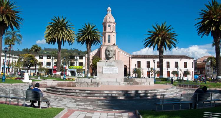 Plaza del pueblo con una estatua y una iglesia al fondo.
