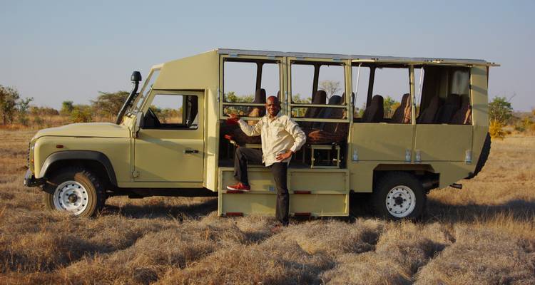 Man standing next to an open safari vehicle in a field