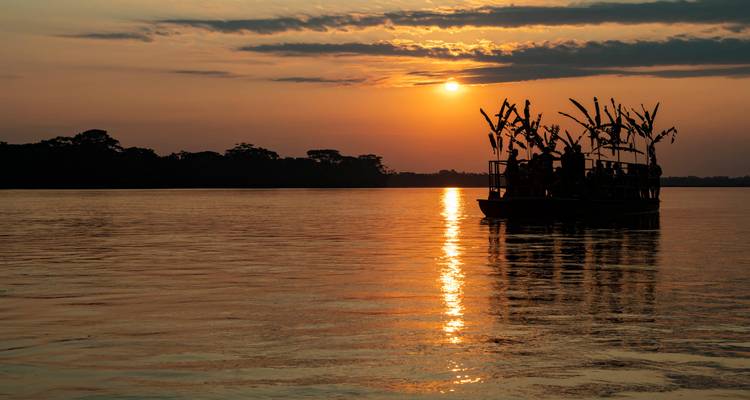Bateau sur la rivière au coucher du soleil avec silhouette d'arbres