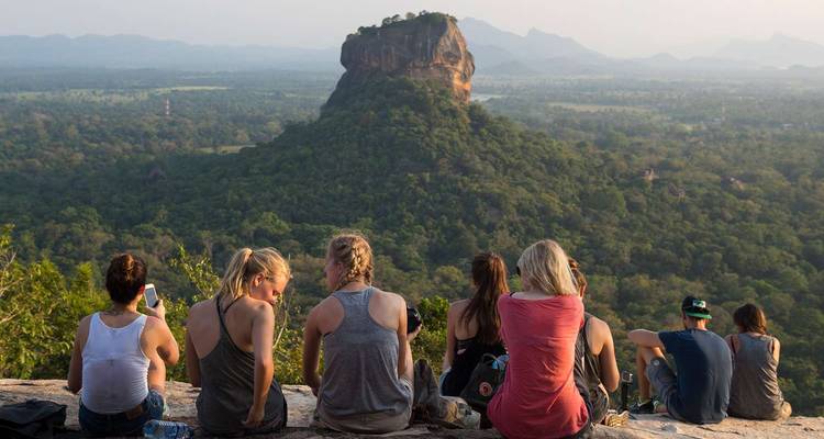 Group of people sitting with a view of Sigiriya rock in the distance.