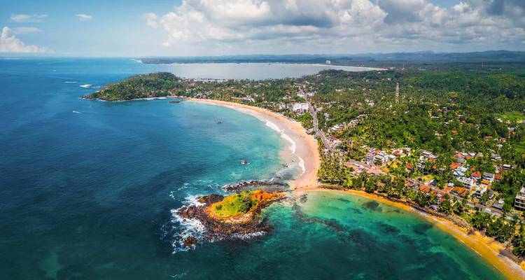 Aerial view of a coastal city with beaches and greenery.
