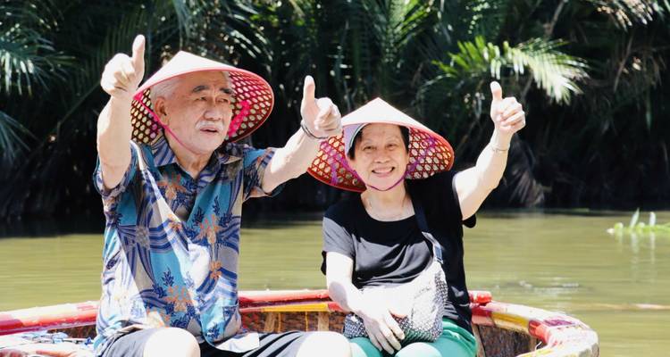 Deux touristes faisant le signe du pouce levé lors d'une promenade en bateau pittoresque avec une végétation luxuriante.