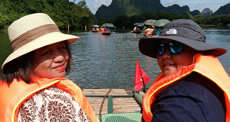 Deux personnes en gilets de sauvetage sur un bateau dans un cadre fluvial pittoresque.