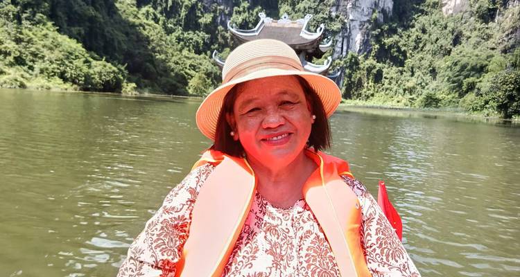 Femme souriante sur un bateau fluvial avec un décor pittoresque de falaises calcaires.