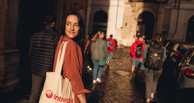 Une jeune femme avec un sac fourre-tout dans une rue pavée avec un groupe qui marche devant.