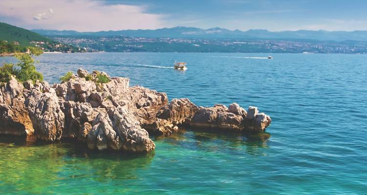 Eau turquoise cristalline de l'Adriatique léchant des rochers calcaires déchiquetés avec un petit bateau et un littoral au loin