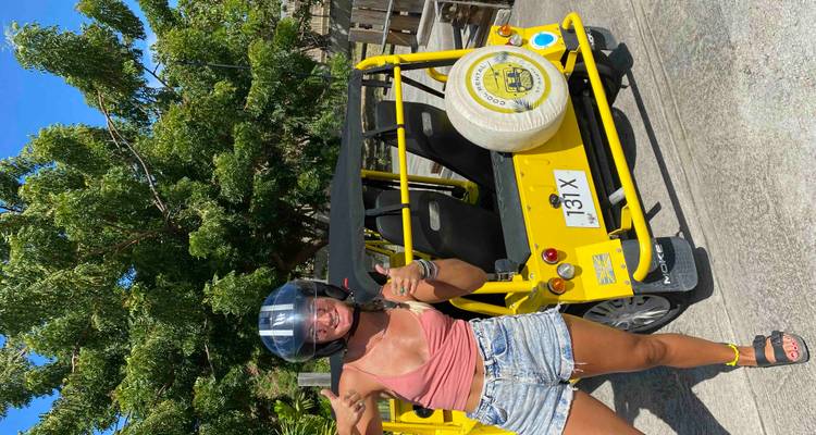 Personne faisant un pouce levé à côté d'un petit véhicule jaune.