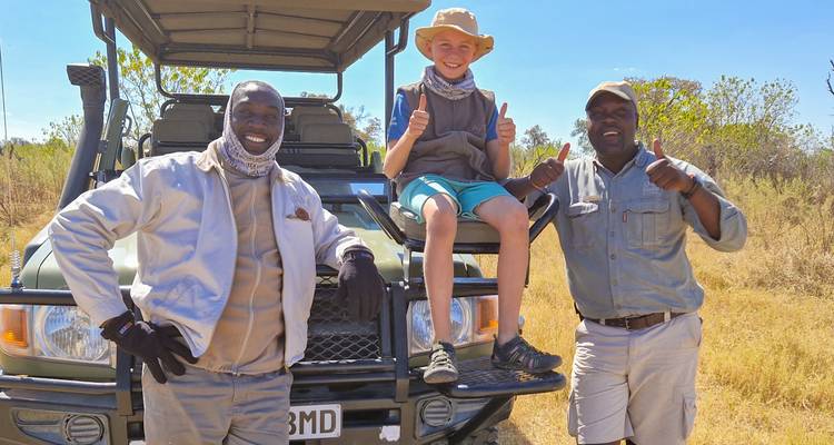 Deux guides et un enfant posant avec un véhicule de safari.