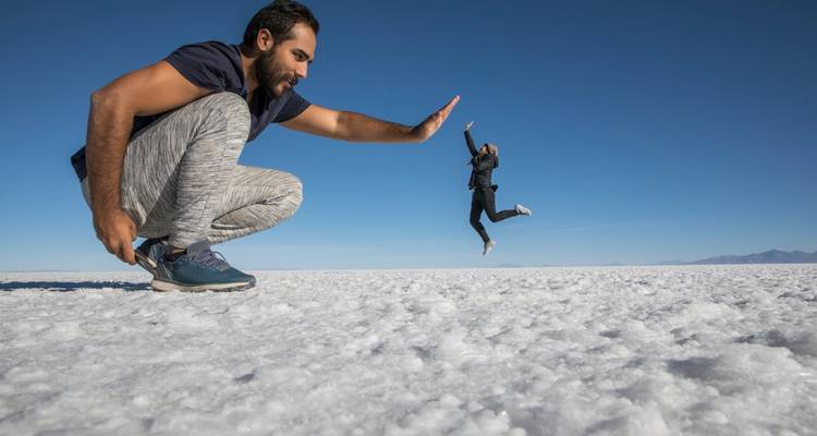 Zwei Personen auf der Uyuni-Salzwüste, eine erscheint groß im Vordergrund und die andere klein in der Ferne.