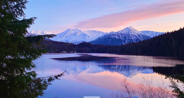 Beautiful sunrise over a calm lake surrounded by snowy mountains.
