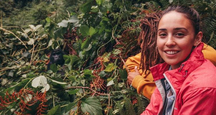 Personne souriante avec un gorille aperçu à travers le feuillage.