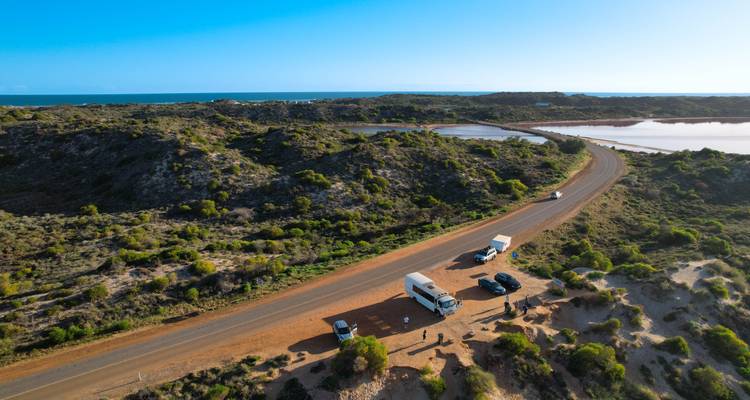 A scenic road with parked vehicles running through a coastal landscape.