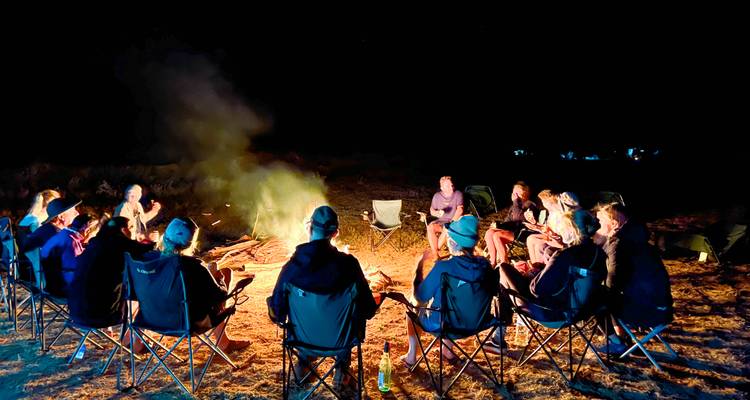 A group of people sitting around a campfire at night.