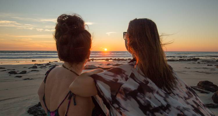 Two women sitting on a beach watching the sunset.
