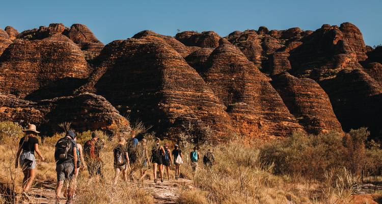 Wandelaars trekken langs de gestreepte bijenkorfdaken van de Bungle Bungles in de late middagzon.