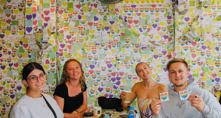 Four people sitting at a cafe table with heart-themed wall decor.