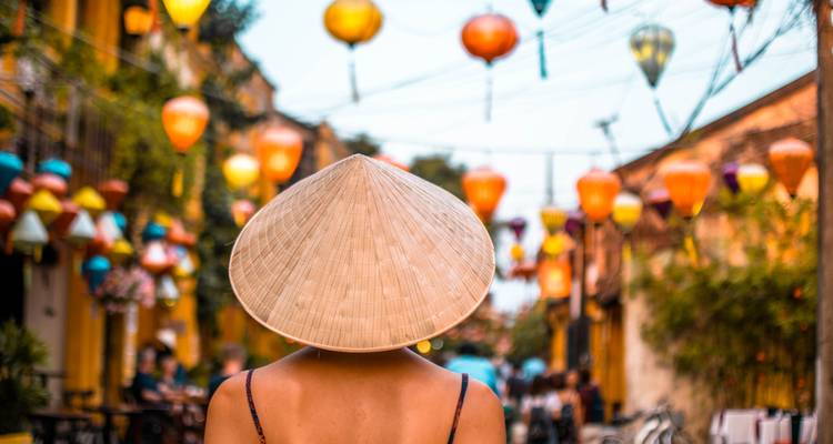 Back view of a person wearing a conical hat under decorative lanterns.