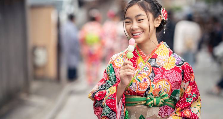 Girl in traditional attire holding a sweet treat, smiling.