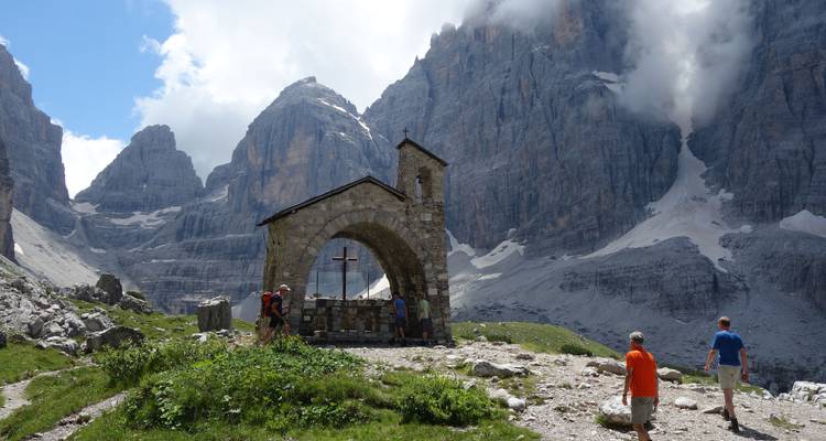 Malerische Landschaft mit einer Steinkapelle und Bergen im Hintergrund.