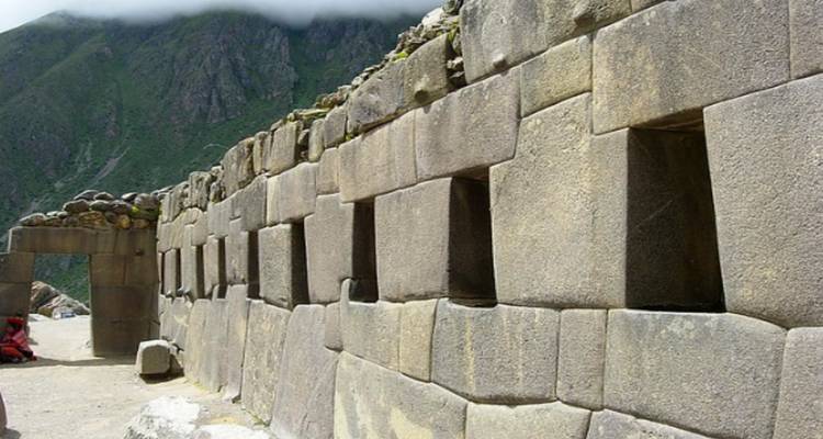 Anciens murs de pierre avec une arche sur un arrière-plan montagneux.