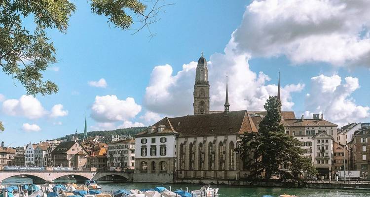 Casco antiguo ribereño de Zúrich con torre de iglesia histórica, botes y nubes esponjosas de verano.