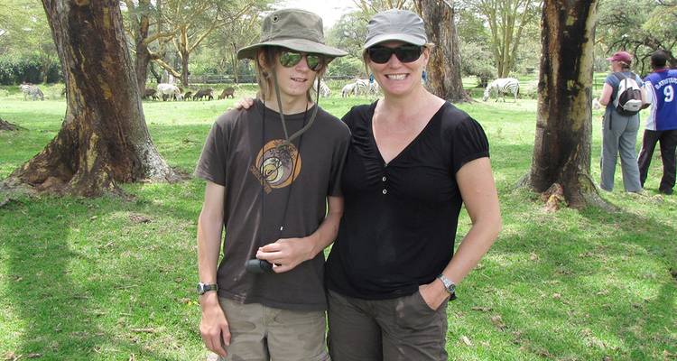 A mother and son standing together with animals grazing in the background.