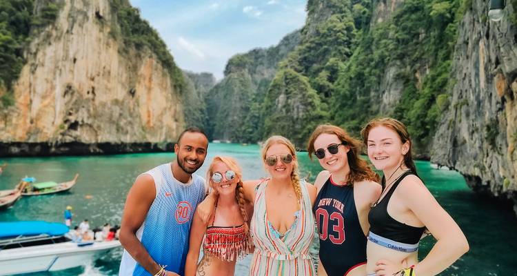 A small group of people standing in front of scenic cliffs and turquoise water.