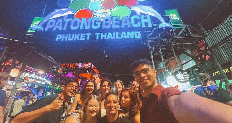 A group of friends taking a selfie under the Patong Beach sign at night.