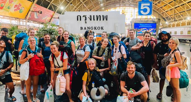 Group of travelers posing in a train station with a sign that reads 'Bangkok'.