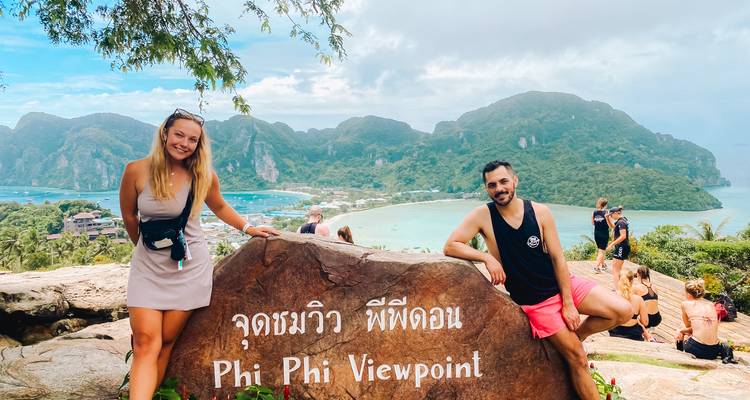 Two people posing by a sign labeled 'Phi Phi Viewpoint' with a scenic landscape in the background.