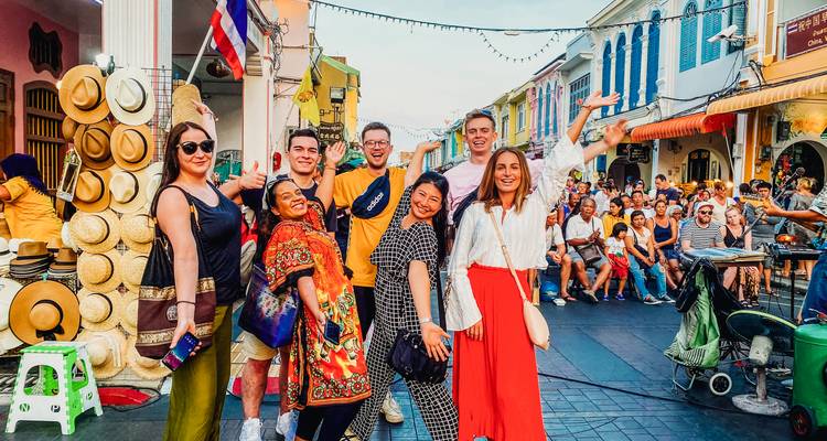 Group of tourists in a vibrant street market with shops and stalls.