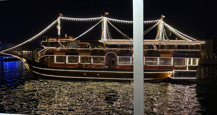 A dhow boat illuminated with lights reflecting on the water at night.