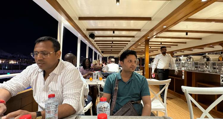 People dining inside a boat with visible buffet setups and city lights in the background.