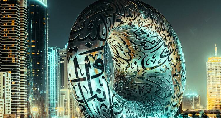 A futuristic building with Arabic script illuminated at night.