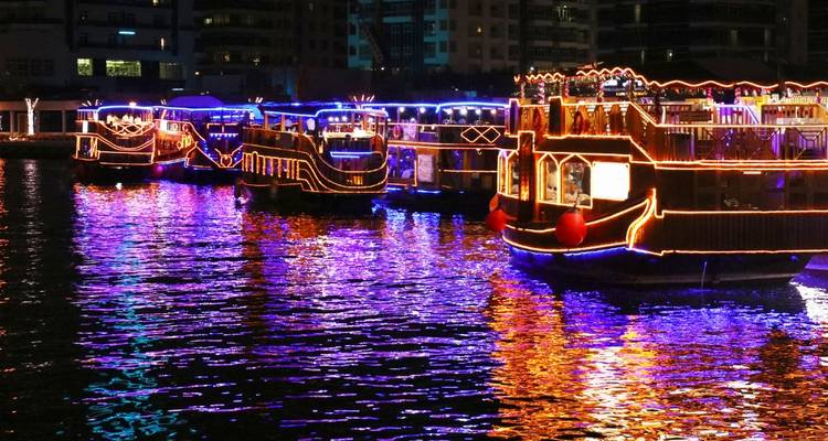 Multiple illuminated dhow boats reflecting on water at night.
