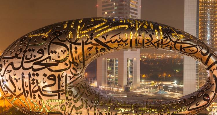 A close-up of a futuristic building with Arabic inscriptions against a city backdrop.