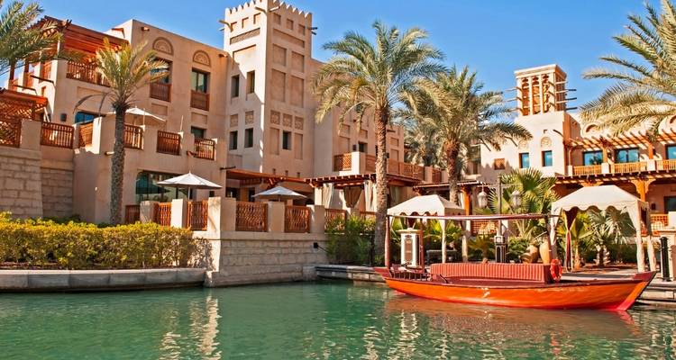 A traditional Middle Eastern building with palm trees and a small boat in a canal.