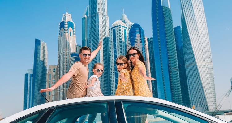 Une famille posant devant l'horizon des gratte-ciel de Dubaï depuis le toit d'un véhicule.