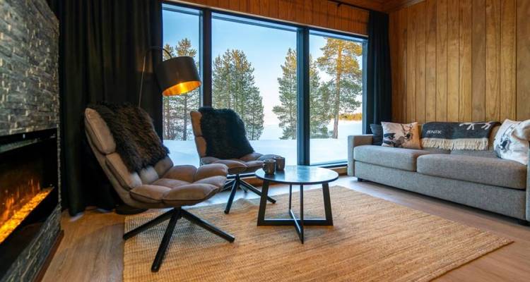 Intérieur de cabane confortable avec des chaises et une vue sur la neige à l'extérieur.