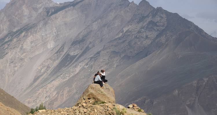Des gens assis sur un rocher avec des montagnes en arrière-plan.