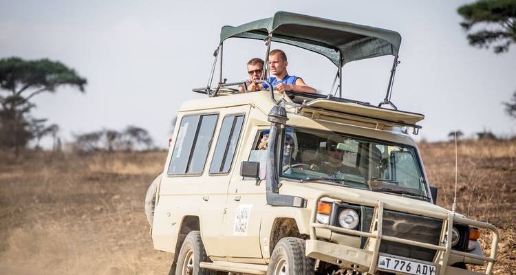 Two people in a safari vehicle driving through a savannah landscape.