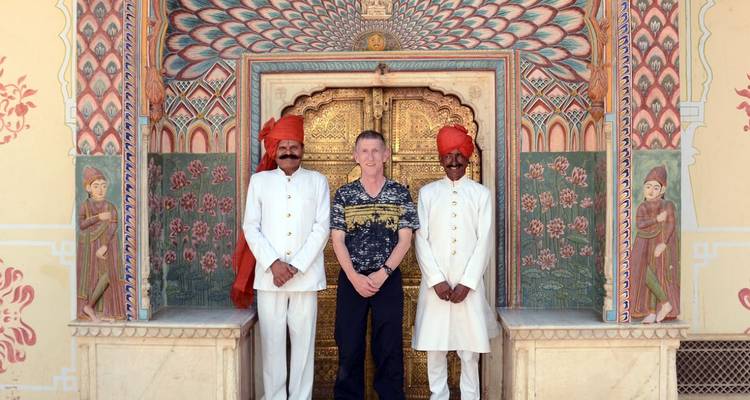 Homme debout avec deux gardes en tenue traditionnelle devant une porte décorée.