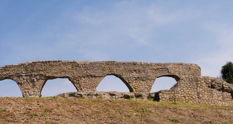 Ruines d'aqueduc en pierre dans un champ herbeux.