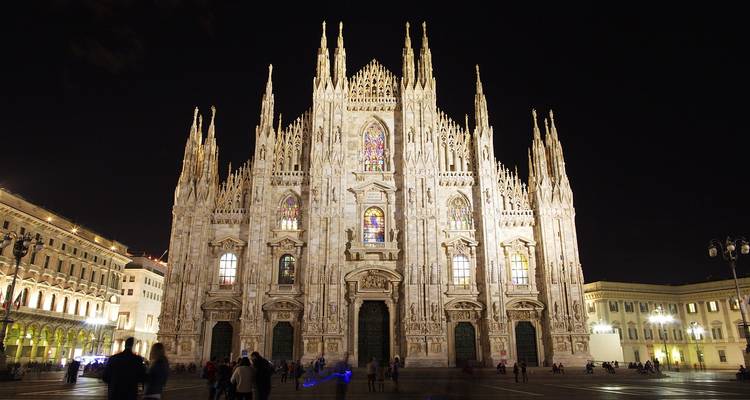 Cathedral under illumination at night with people in the foreground.