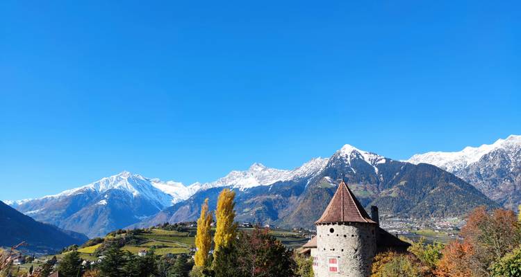 Autumn landscape with castle tower and snowcapped mountains.