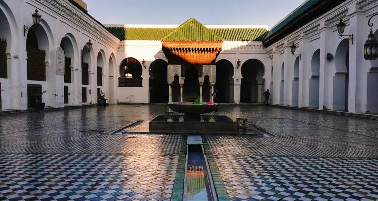 Cour d'un bâtiment marocain traditionnel avec sol carrelé et fontaine.