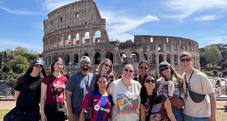Groupe de touristes souriants posant devant les ruines du Colisée sous un ciel lumineux