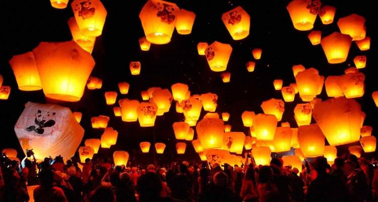 Numerous brightly lit lanterns floating in the night sky.