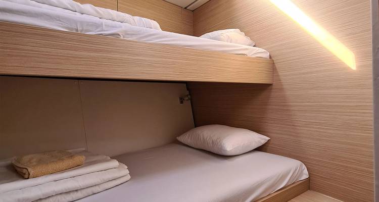 Cabine de yacht compacte avec lits superposés habillés de draps blancs frais.