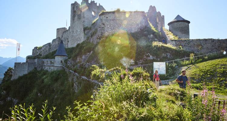 Zwei Personen gehen in der Nähe antiker Ruinen mit Sonnenblendung.
